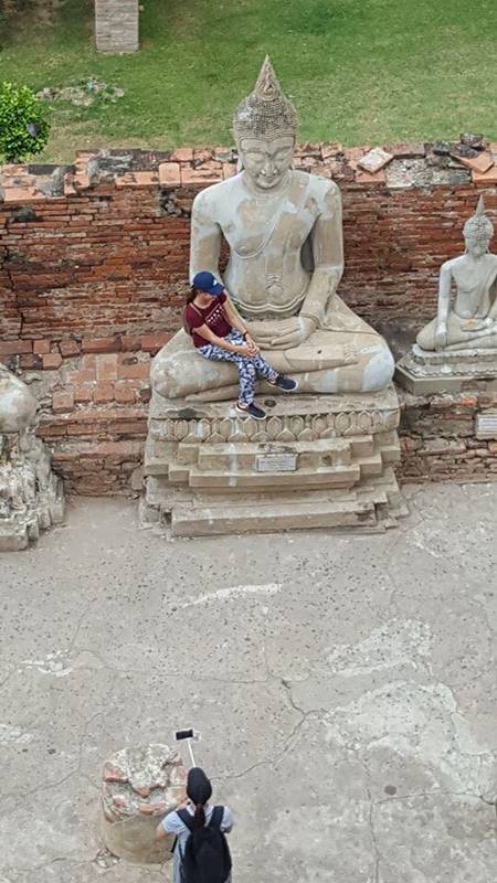 นักท่องเที่ยวสาวนั่งบนพระพุทธรูป