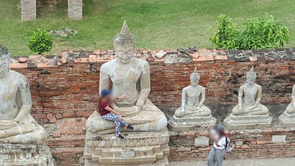 นักท่องเที่ยวสาวนั่งบนพระพุทธรูป